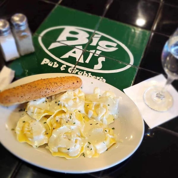 Big Al's Pub & Grubberia's ravioli with cream sauce and a breadstick, on a black tiled table.