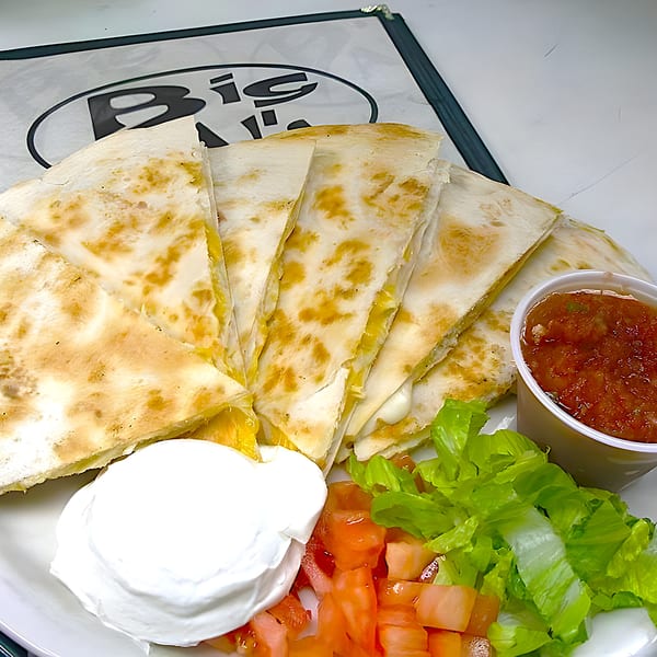 Big Al's quesadilla with salsa, sour cream, lettuce, and diced tomatoes on a white plate.