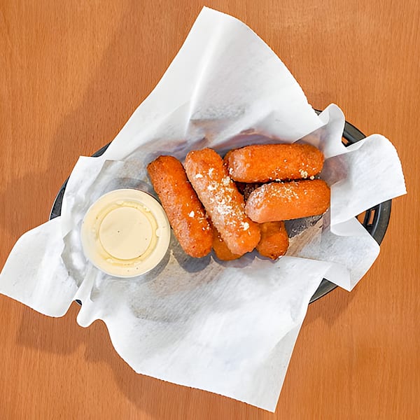 Fried cheese sticks with powdered sugar and a side of dipping sauce in a basket.