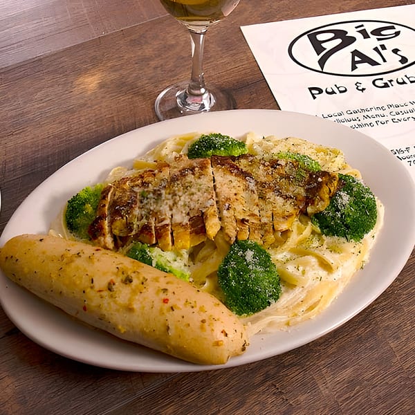 Chicken alfredo with broccoli and a breadstick on a white plate, with a Big Al's menu in the background.